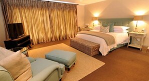 A hotel room with a bed, two bedside tables, a TV, a sofa, and a large window with curtains. - 8A Grahamstown (Makhanda)