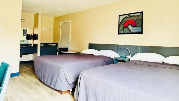 A hotel room with two beds, a desk, a chair, and a bathroom. - Plains Motor Inn (Stettler)