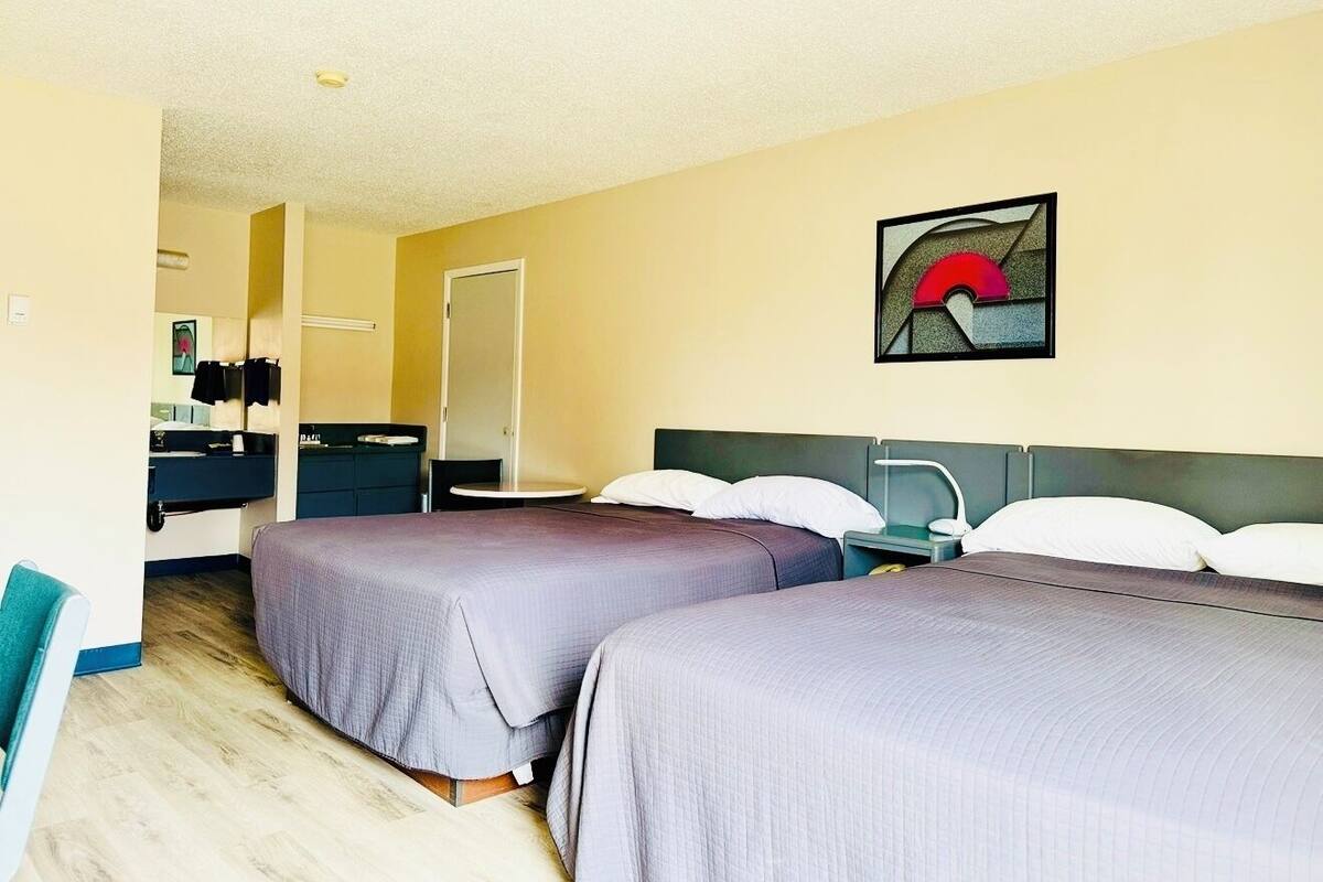 A hotel room with two beds, a desk, a chair, and a bathroom.