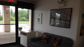 A reception area with a couch, a desk, and a framed photo on the wall. - Plains Motor Inn (Stettler)