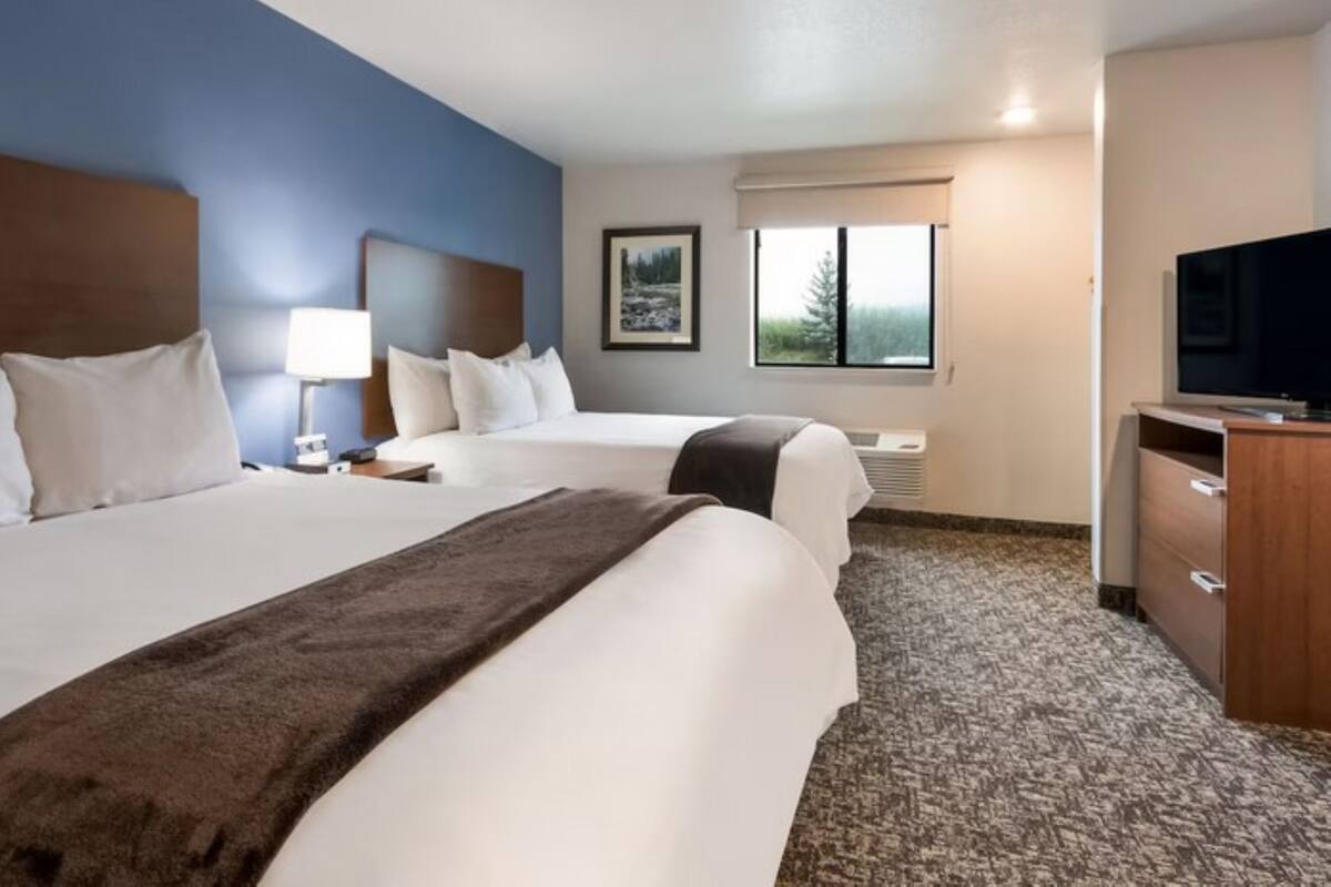 A hotel room with two beds, a TV, a desk, a lamp, a window with a view, and a painting on the wall.