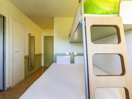 Uma cama beliche com escada de madeira, colchão branco e cortina verde em quarto com piso de madeira e porta branca.
