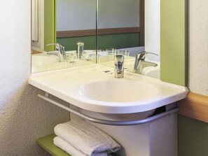 A bathroom with a white sink, two faucets, and a mirror. - ibis budget Saint Gratien Enghien les Bains (Saint-Gratien)