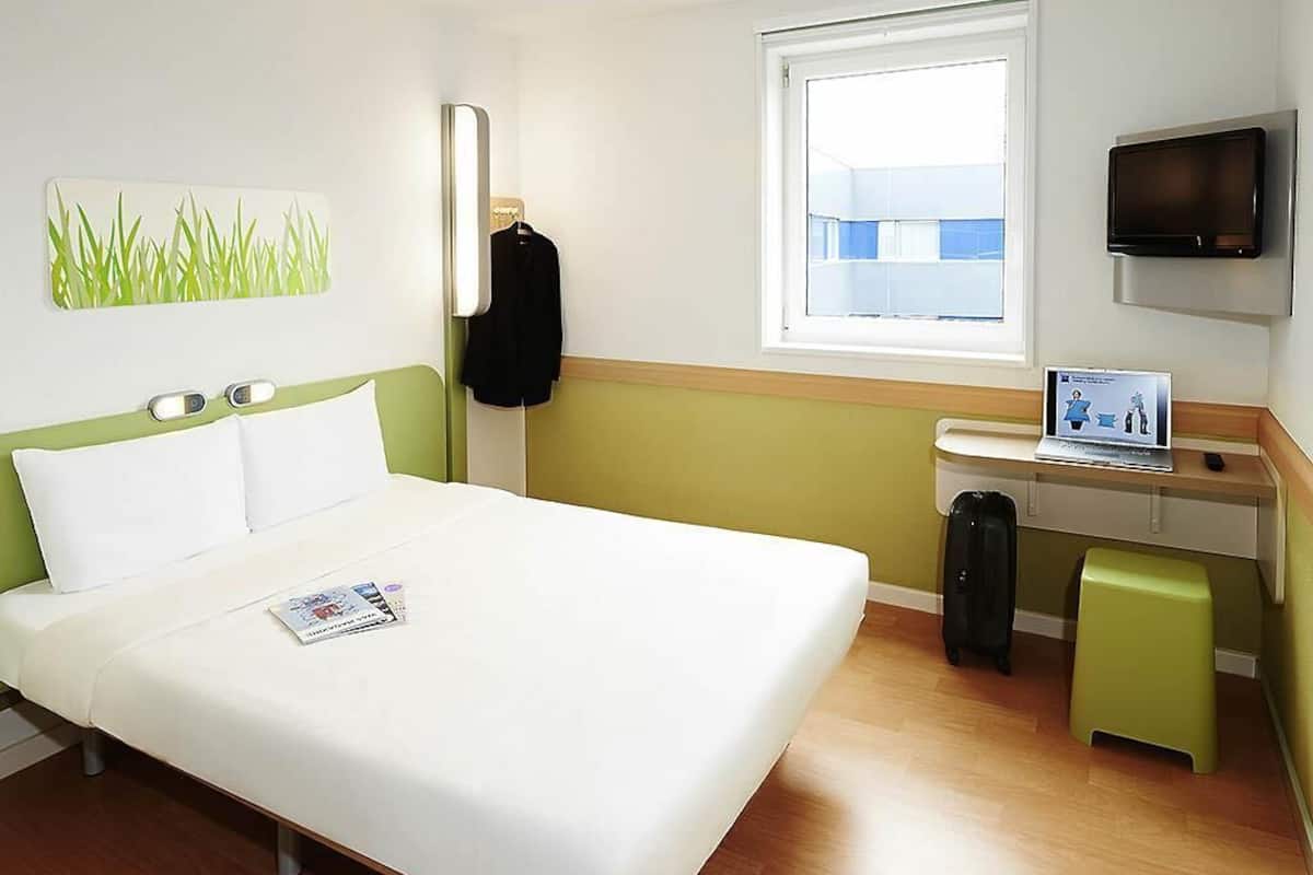 Una habitació d'hotel amb un llit, un escriptori amb un ordinador, una televisió i una finestra.