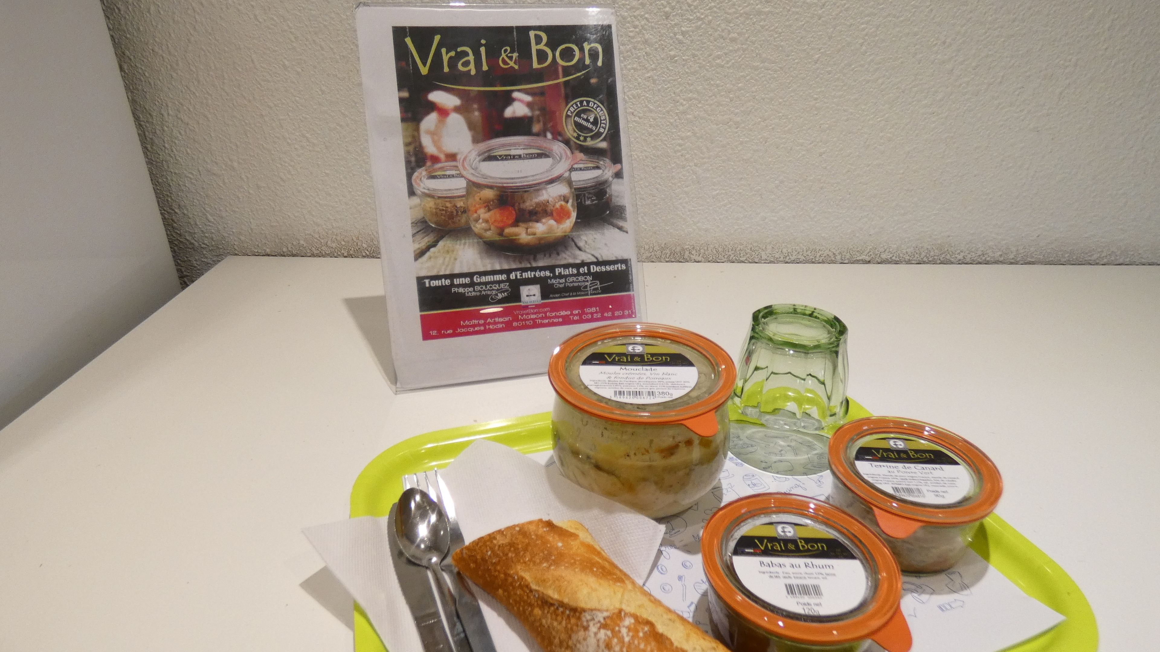 A table with a sign for 'Vrai & Bon' and three jars of food on a green plate.