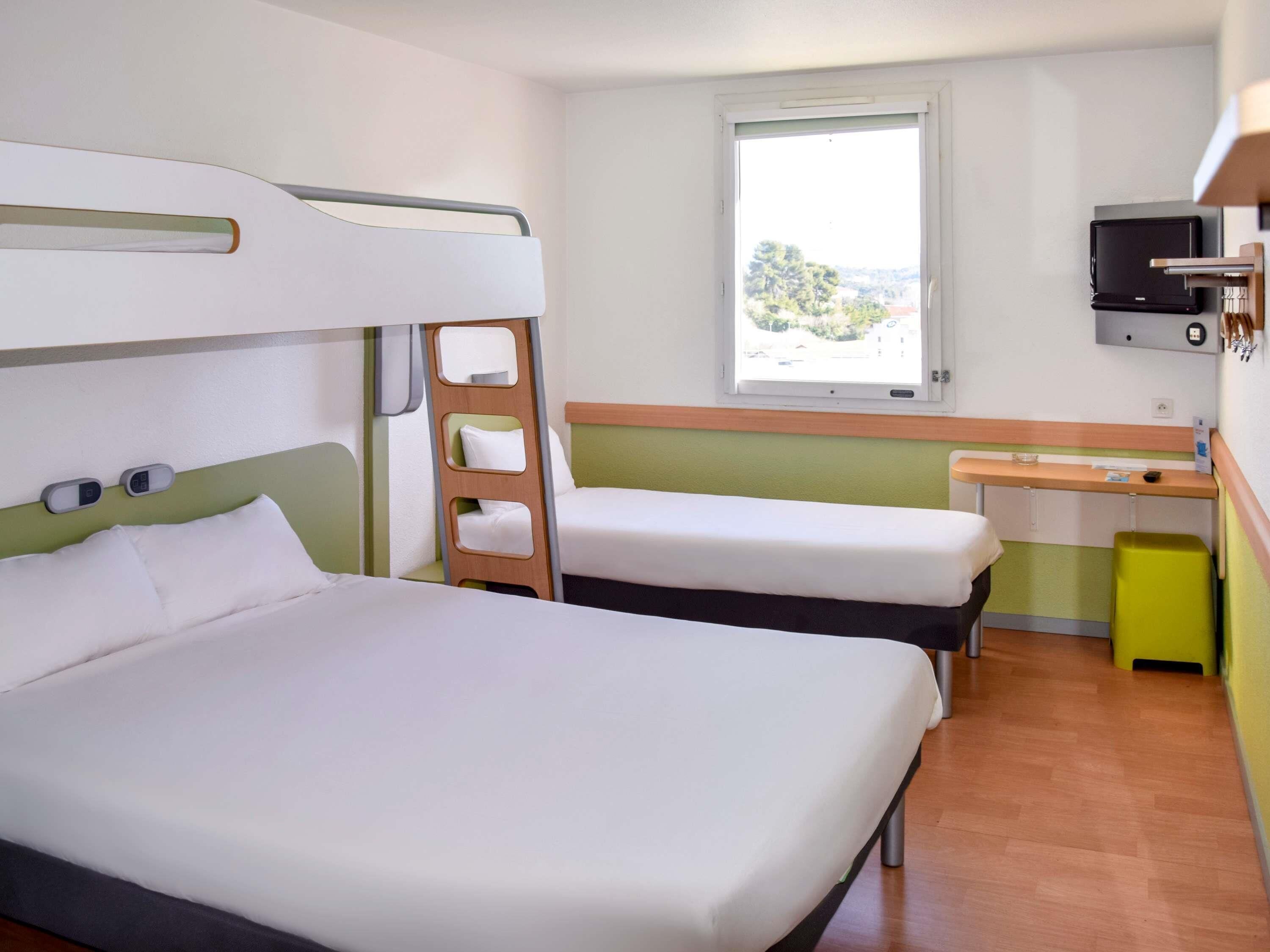 Habitación de hotel con dos camas, un escritorio, un televisor y una ventana con vistas.