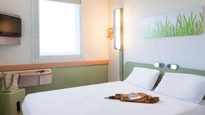 Hotelkamer met een bed, een raam, een aan de muur bevestigde televisie en een schilderij van gras.