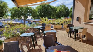 Een buitenpatio met tafels en stoelen, omringd door potplanten en uitzicht op geparkeerde auto's en gebouwen.