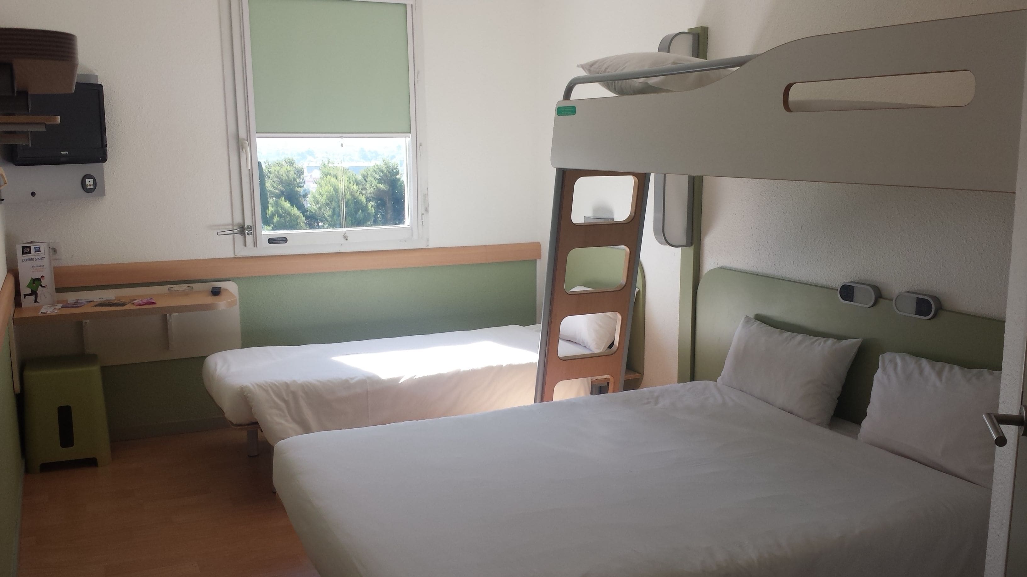Una habitación pequeña y limpia con dos camas, un escritorio y una ventana.