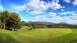 Een golfbaan met een heldere lucht, bomen en bergketens in de verte.