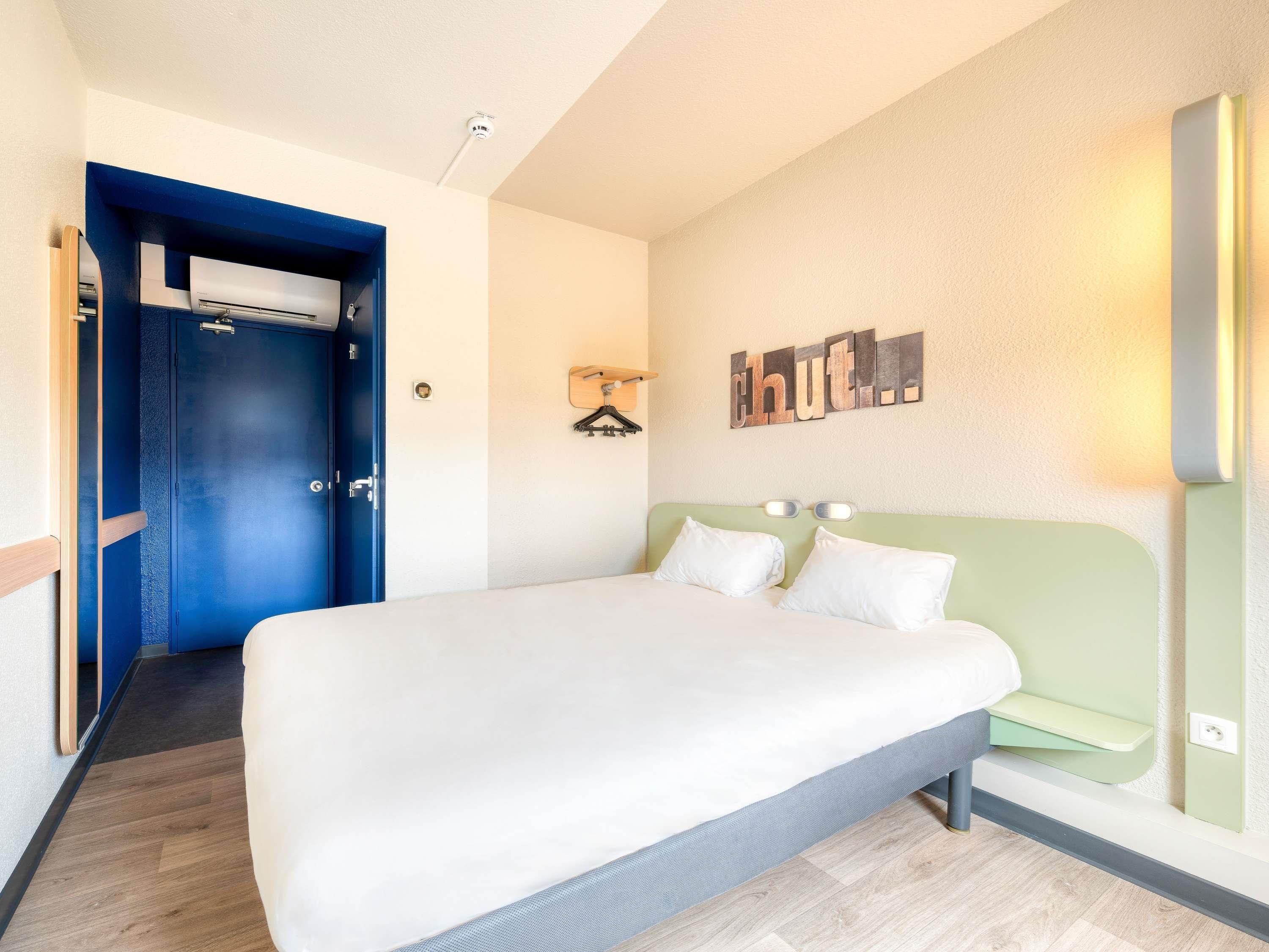 A hotel room with a bed, a wardrobe, a wall-mounted light, and a coat rack.