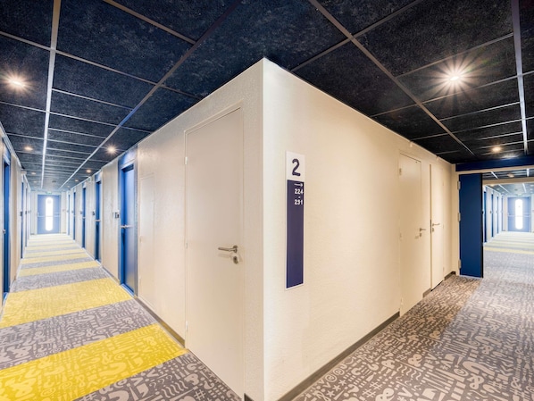 A hotel corridor with a row of rooms, a number sign indicating room 2, and a patterned carpet. - ibis budget Versailles Trappes (Trappes)