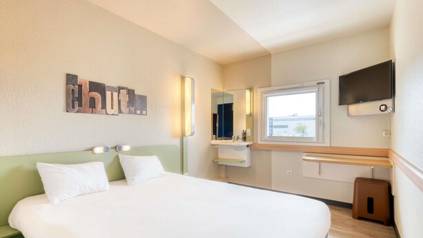 Une chambre d’hôtel avec un lit, un miroir, une télévision et une fenêtre.