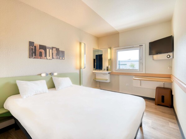A hotel room with a bed, a mirror, a TV, and a window. - ibis budget Versailles Trappes (Trappes)