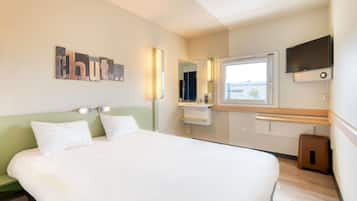 Une chambre d’hôtel avec un lit, un miroir, une télévision et une fenêtre.