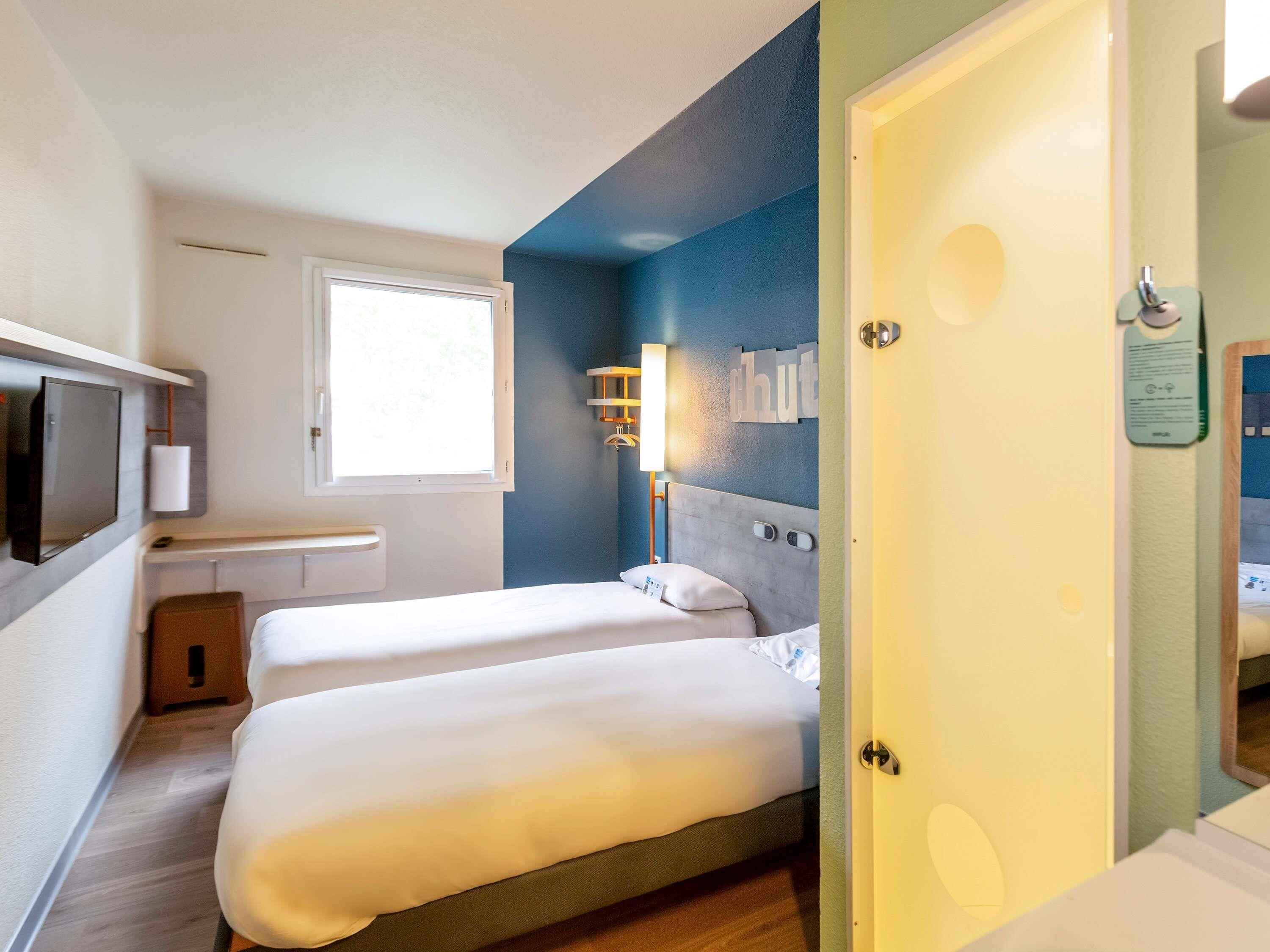 A hotel room with two beds, a TV, a desk, and a window.
