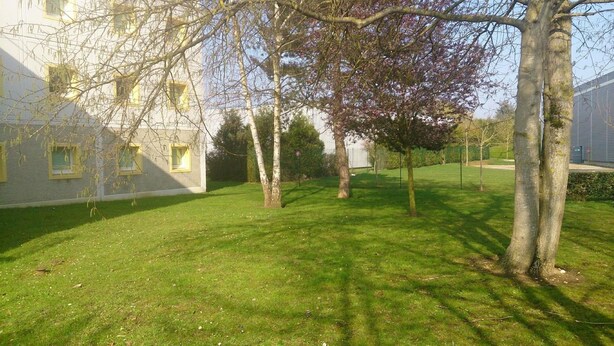 A grassy courtyard with trees and a building with multiple windows. - ibis budget Versailles Trappes (Trappes)