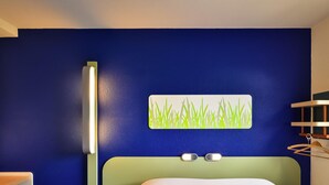 Una habitación de hotel con cama, mesita de noche, lámpara y una obra de arte colgada en la pared.