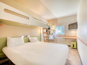 A compact hotel room with a bed, a small bathroom, a TV, and a window. - ibis budget Versailles Trappes (Trappes)