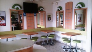 Un restaurant avec des banquettes et des tabourets hauts, un téléviseur fixé au mur et un miroir qui reflète l’intérieur.