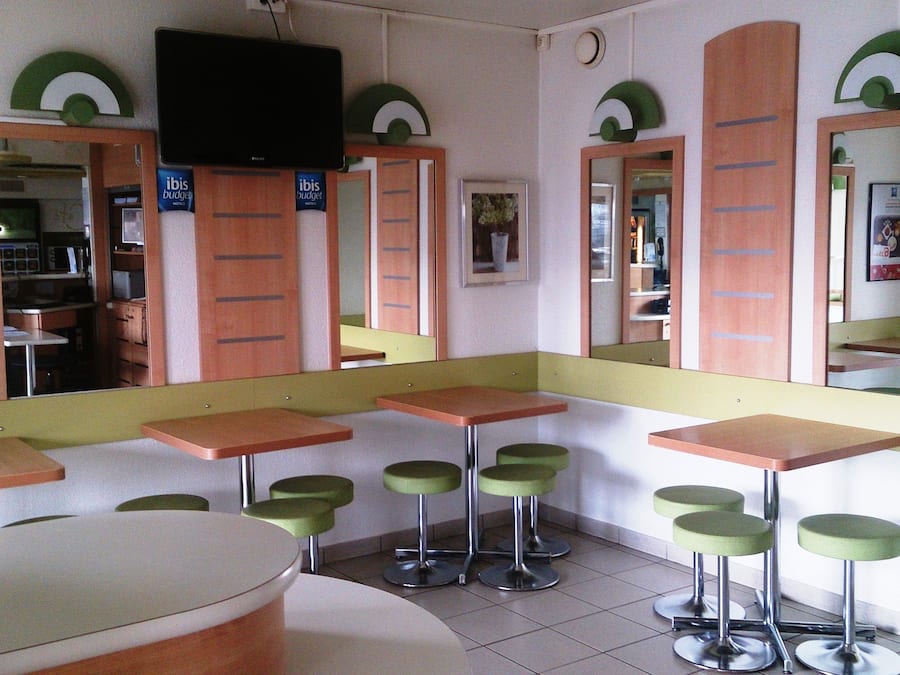 A restaurant with booths and high stools, a TV mounted on the wall, and a mirror reflecting the interior.