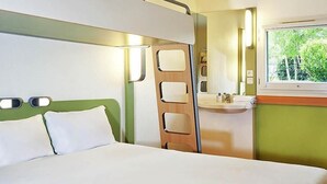 Un dormitorio con cama, ventana, espejo y baño con lavamanos.