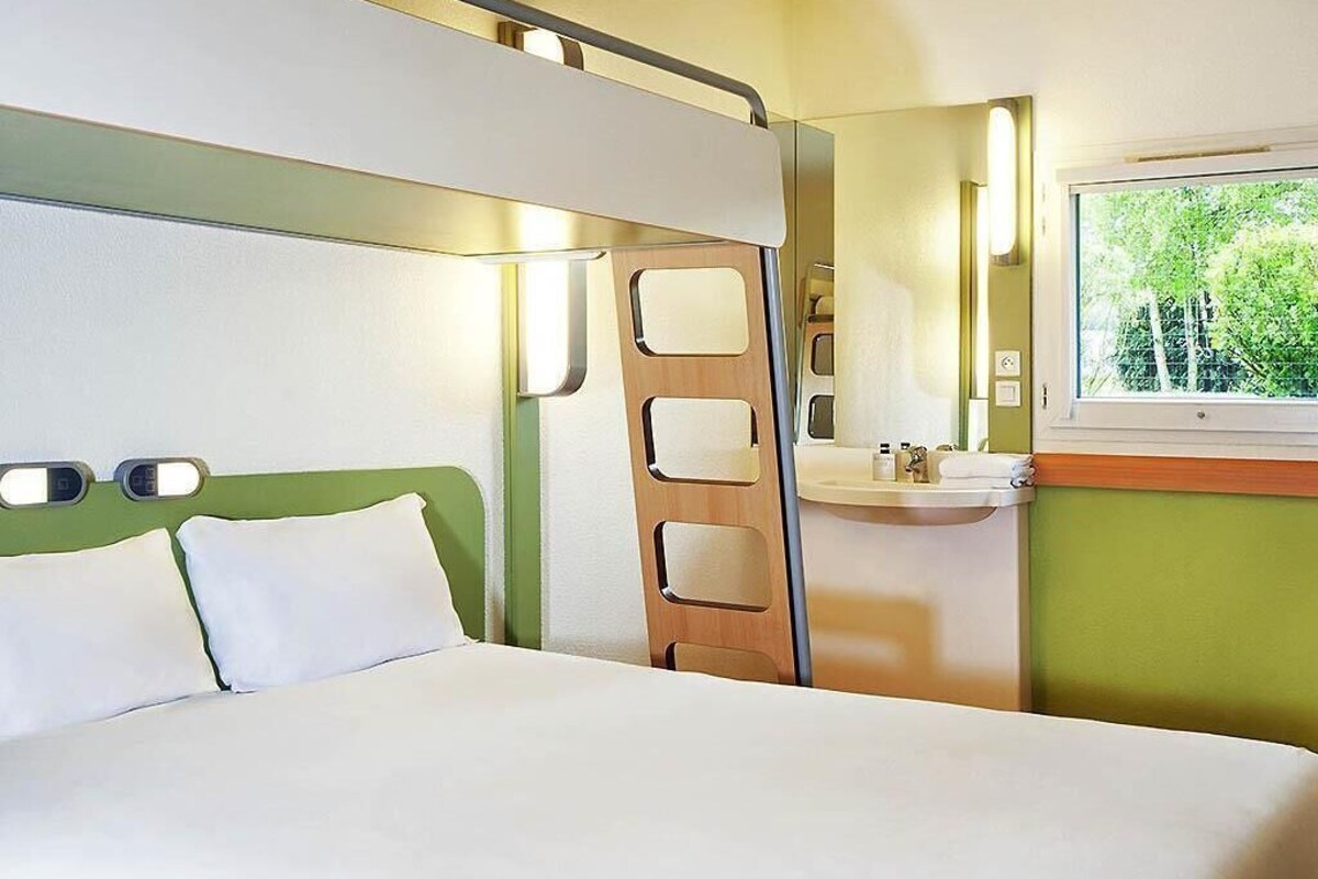A bedroom with a bed, a window, a mirror, and a bathroom with a sink.