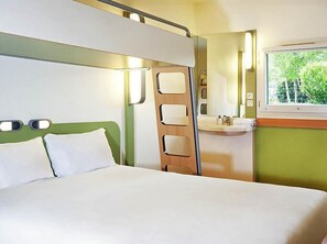 A bedroom with a bed, a window, a mirror, and a bathroom with a sink. - ibis budget Versailles Trappes (Trappes)