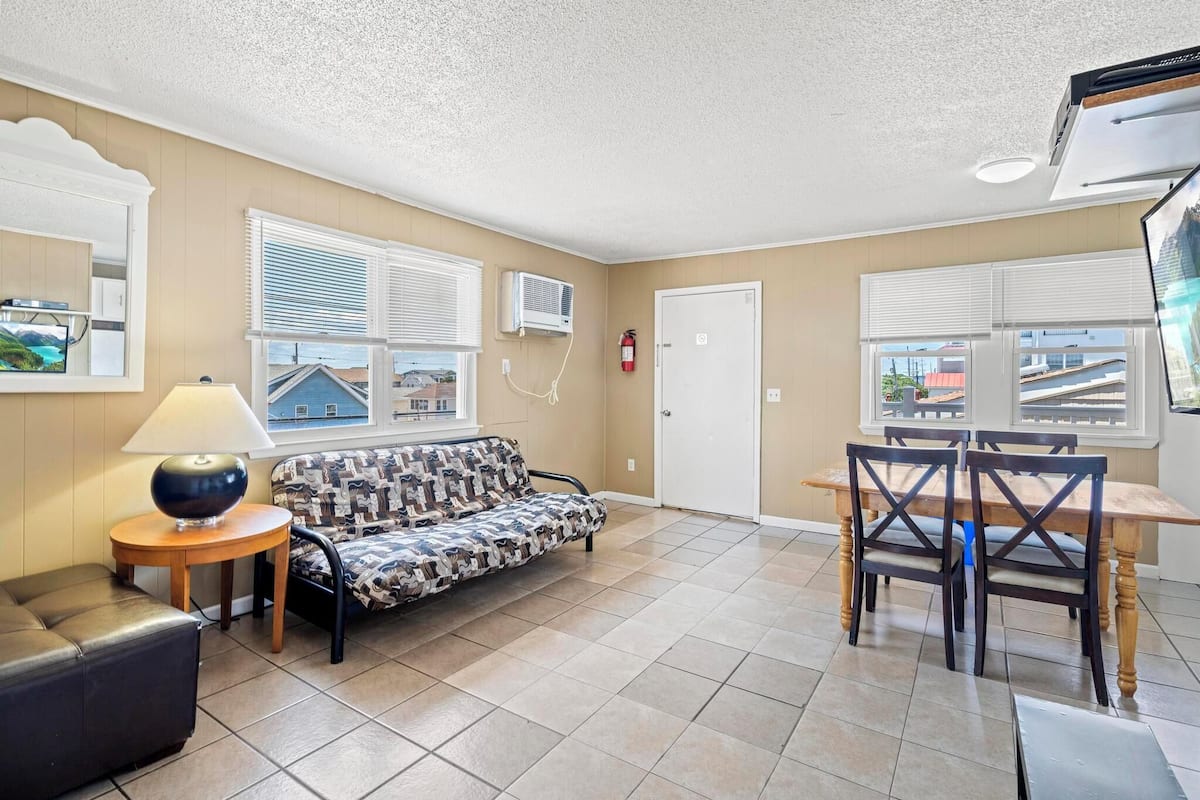 A room with a sofa, a table with chairs, a lamp, and a fire extinguisher.