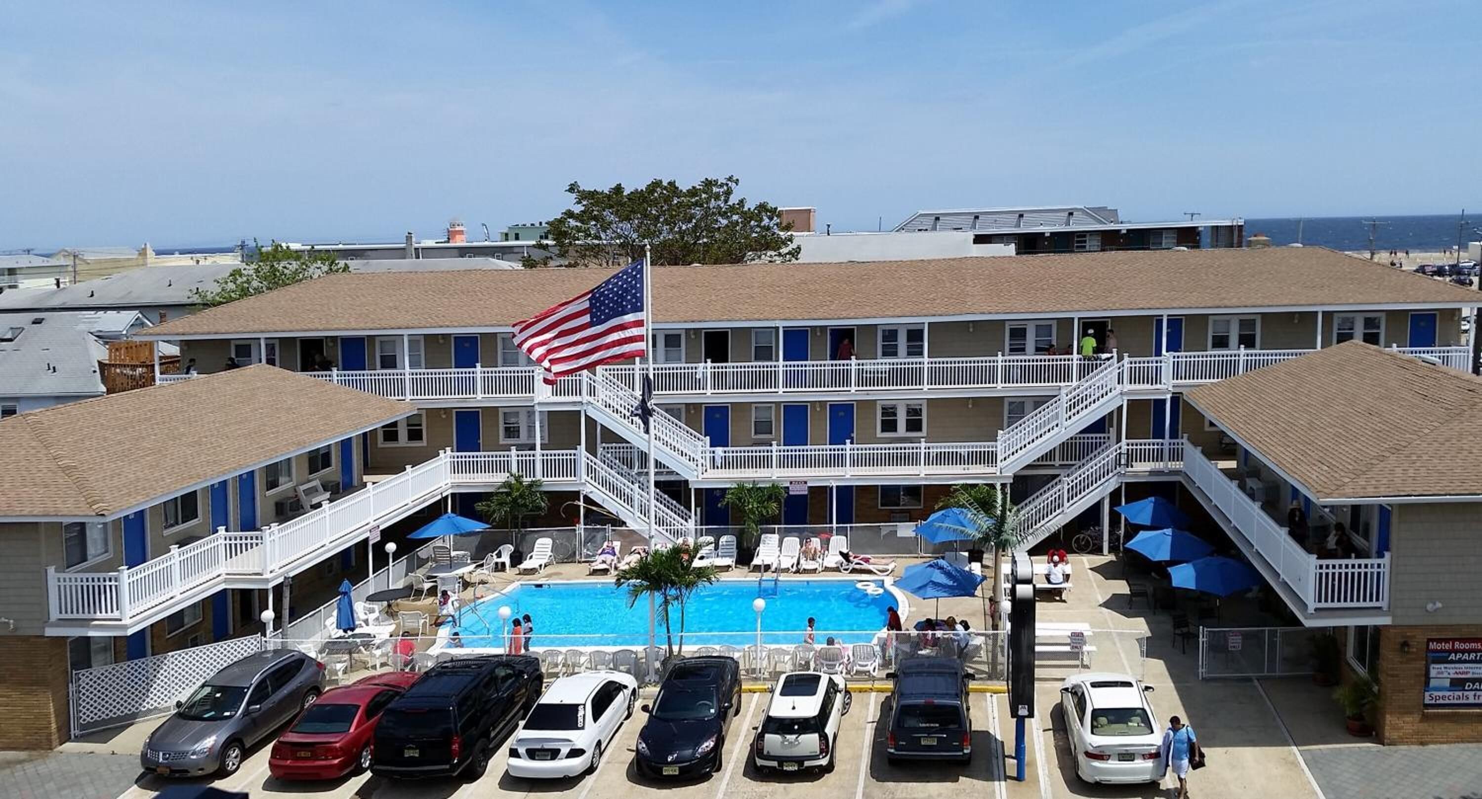 A motel with a swimming pool, multiple balconies, and a flag.