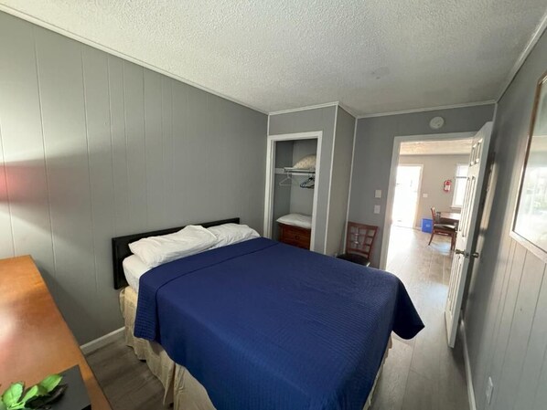 A bedroom with a bed, a bedside table, a wardrobe, and a door leading to another room.