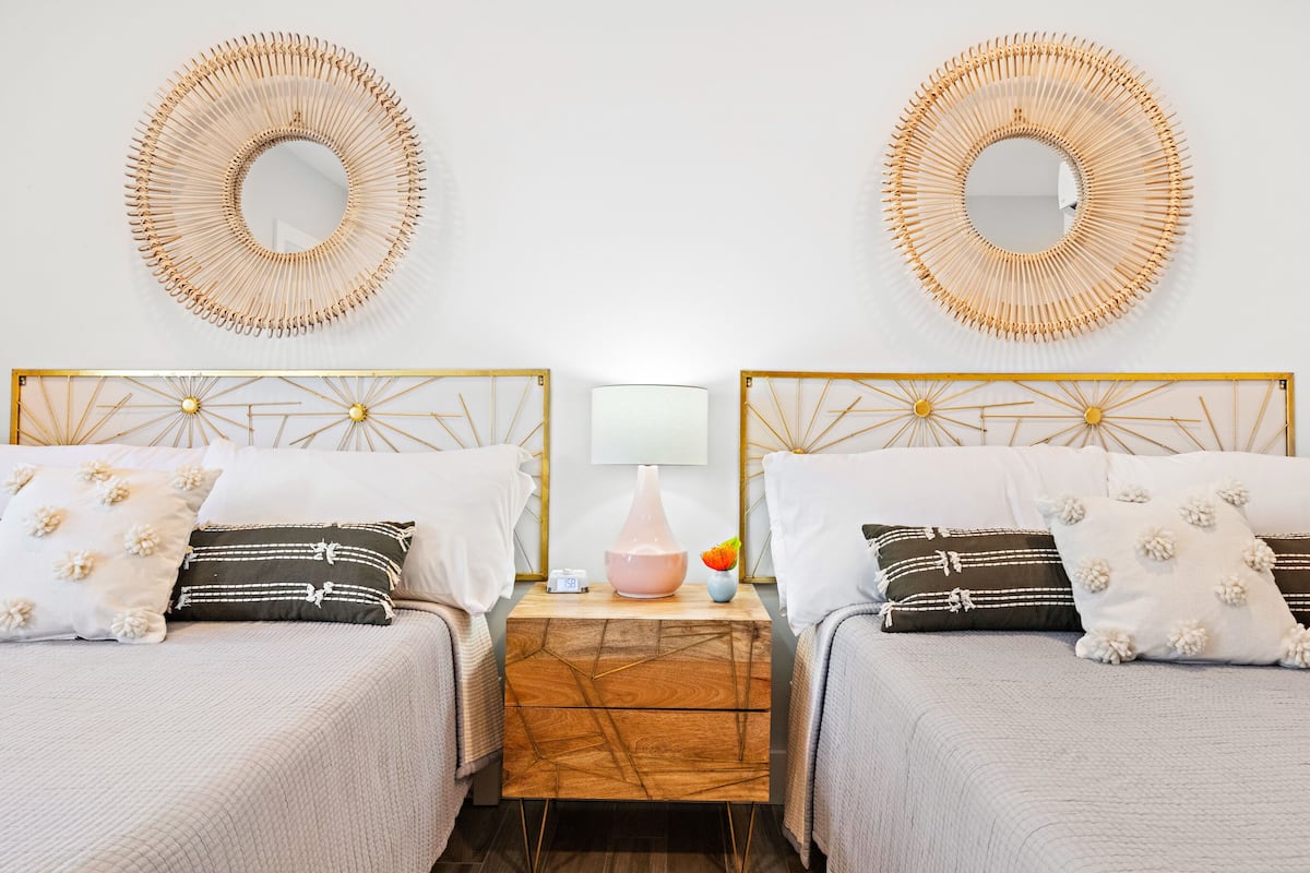 A hotel room with two beds, a nightstand with a lamp, and two wall-mounted mirrors.