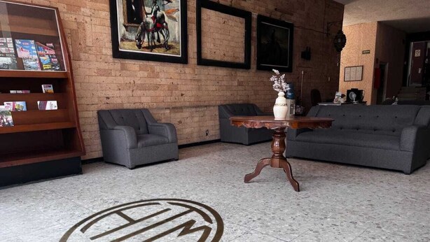 Un vestíbulo con suelo de mármol, sofás grises, una mesa de madera y una estantería con revistas.
