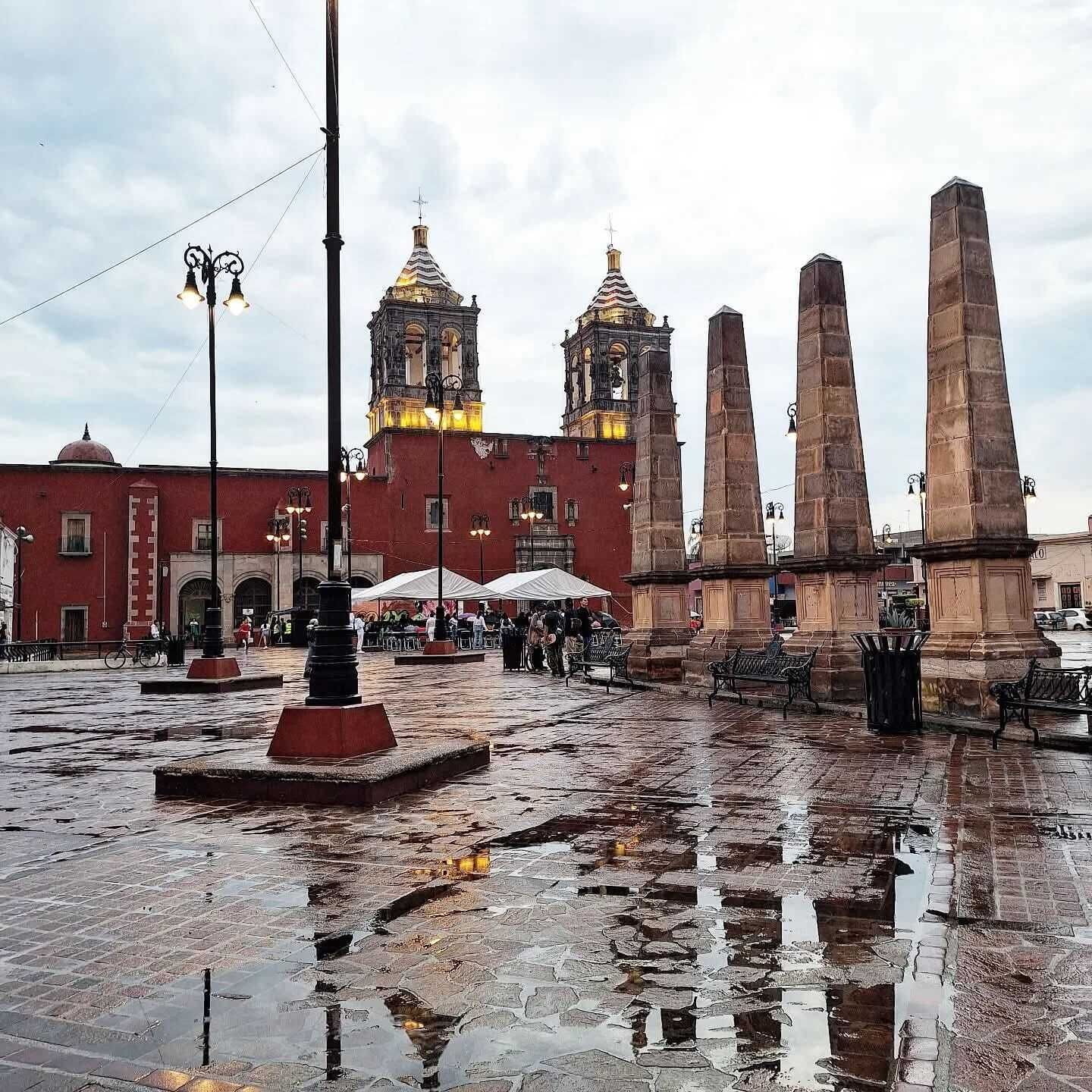 A plaza with a historic building, a fountain, and a statue.