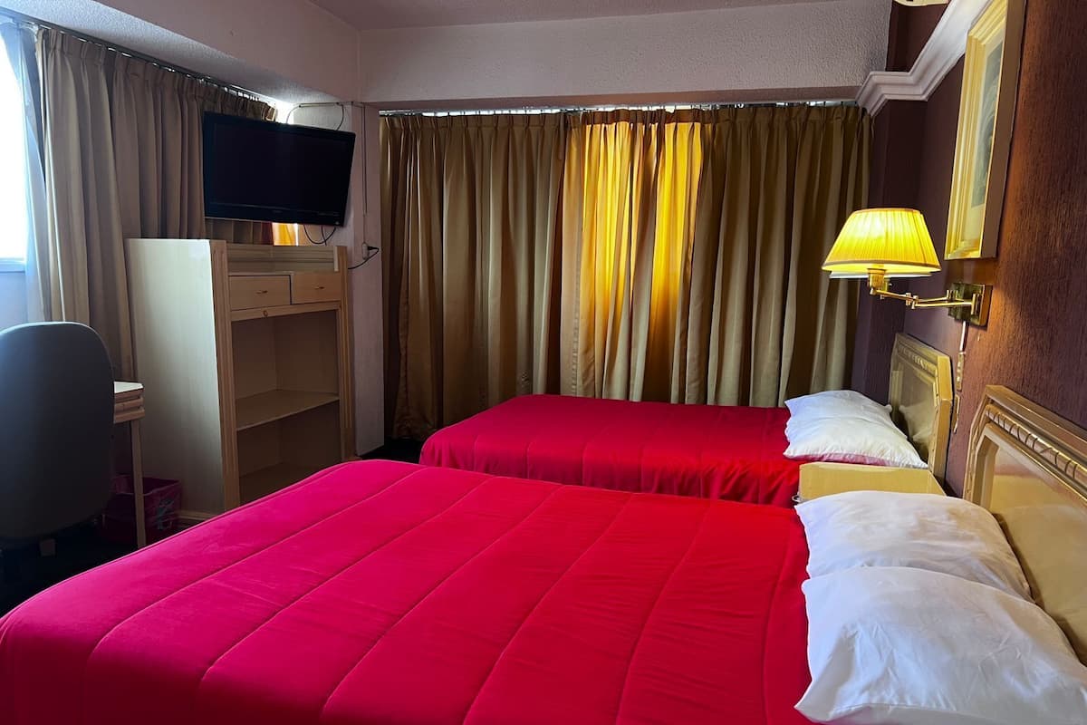 Een hotelkamer met twee bedden, een bureau, een televisie en een lamp.