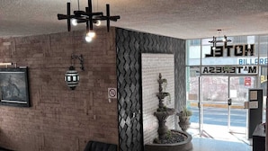 Un vestíbulo con pared de ladrillo, un sofá negro, una fuente decorativa y un cartel que dice 'HOTEL AMESTAS'.