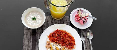 Une table dressée avec un repas composé d’un bol de soupe, d’une assiette de pâtes à la sauce tomate et au fromage, d’un verre de jus d’orange et d’une assiette de crème glacée.
