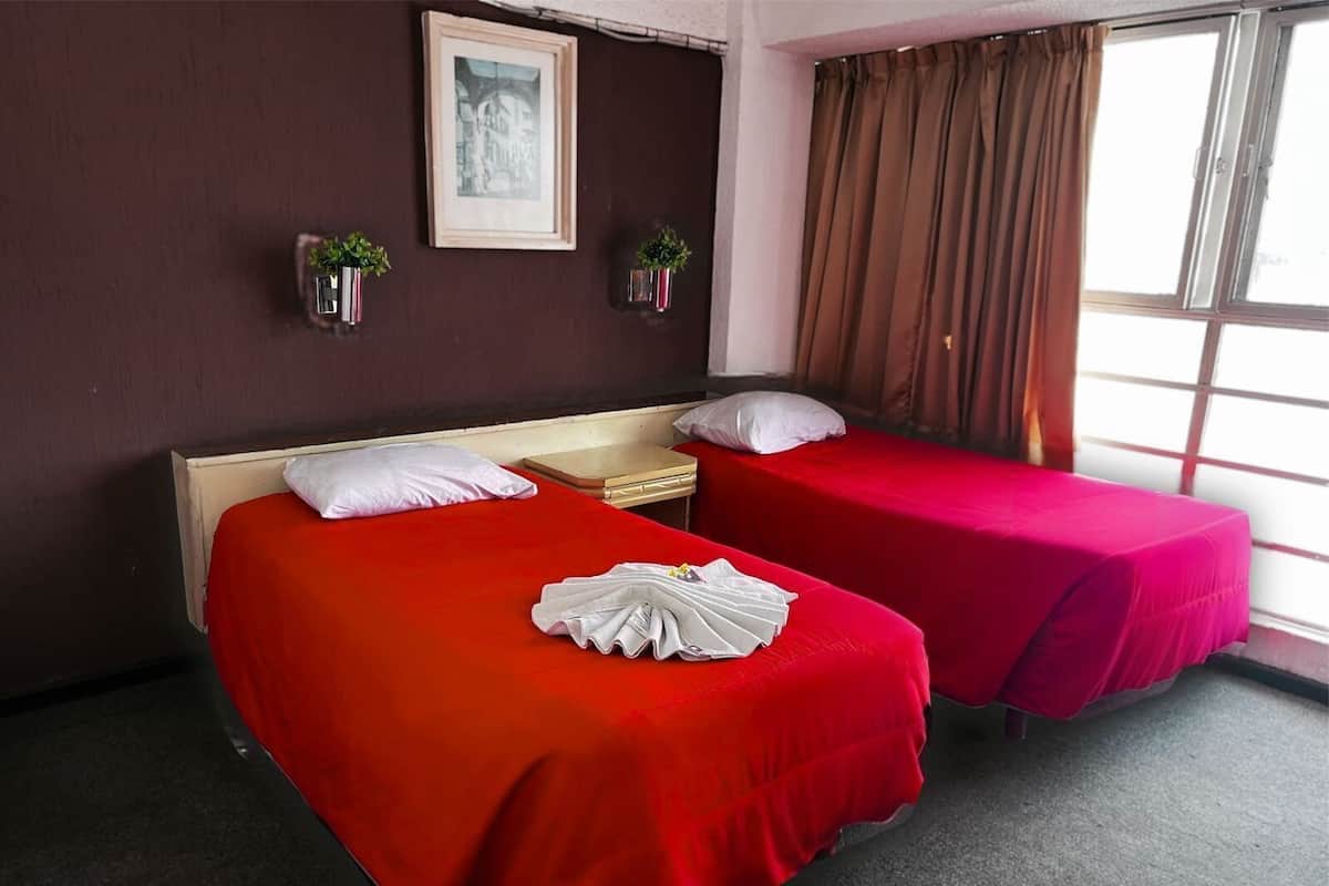 Een hotelkamer met twee bedden, een nachtkastje, een inlijsting foto aan de muur en een raam met gordijnen.