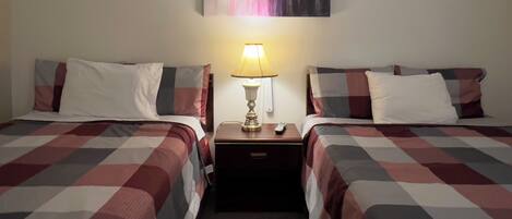 Habitación de hotel con dos camas, cada una con una colcha a cuadros, una mesita de noche con lámpara y un cuadro en la pared.
