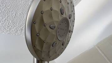 A showerhead with multiple nozzles, attached to a metal pipe, in a bathroom with white walls and a white bathtub.
