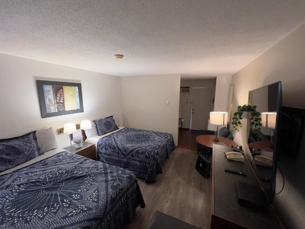 Habitación de hotel con dos camas, un escritorio con computadora, un televisor y una puerta que da a un baño.