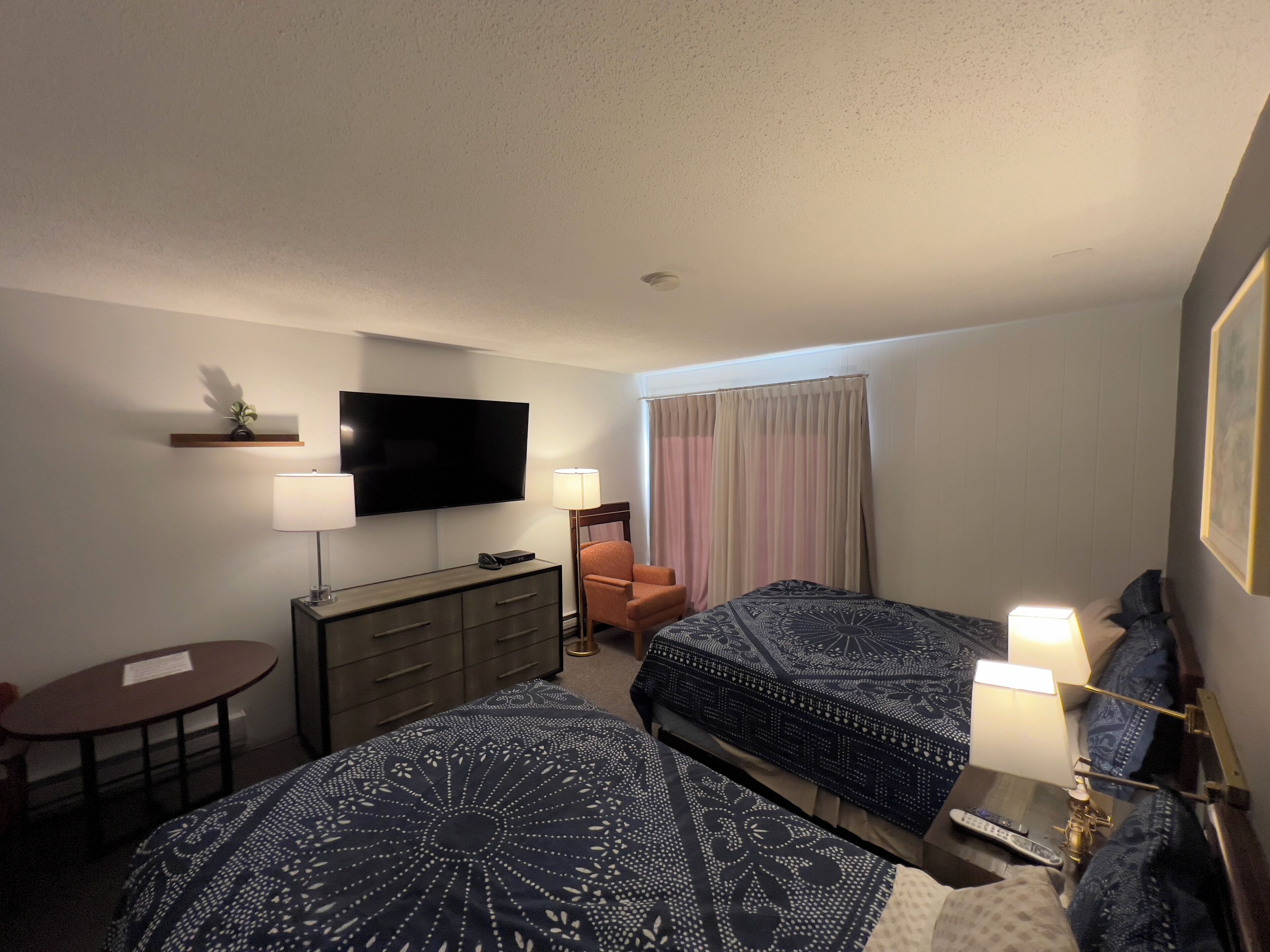 A hotel room with two beds, a TV, a desk, a chair, and a window with curtains.