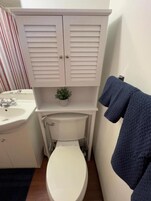 Un baño con inodoro blanco, lavamanos y un mueble con una pequeña planta encima.