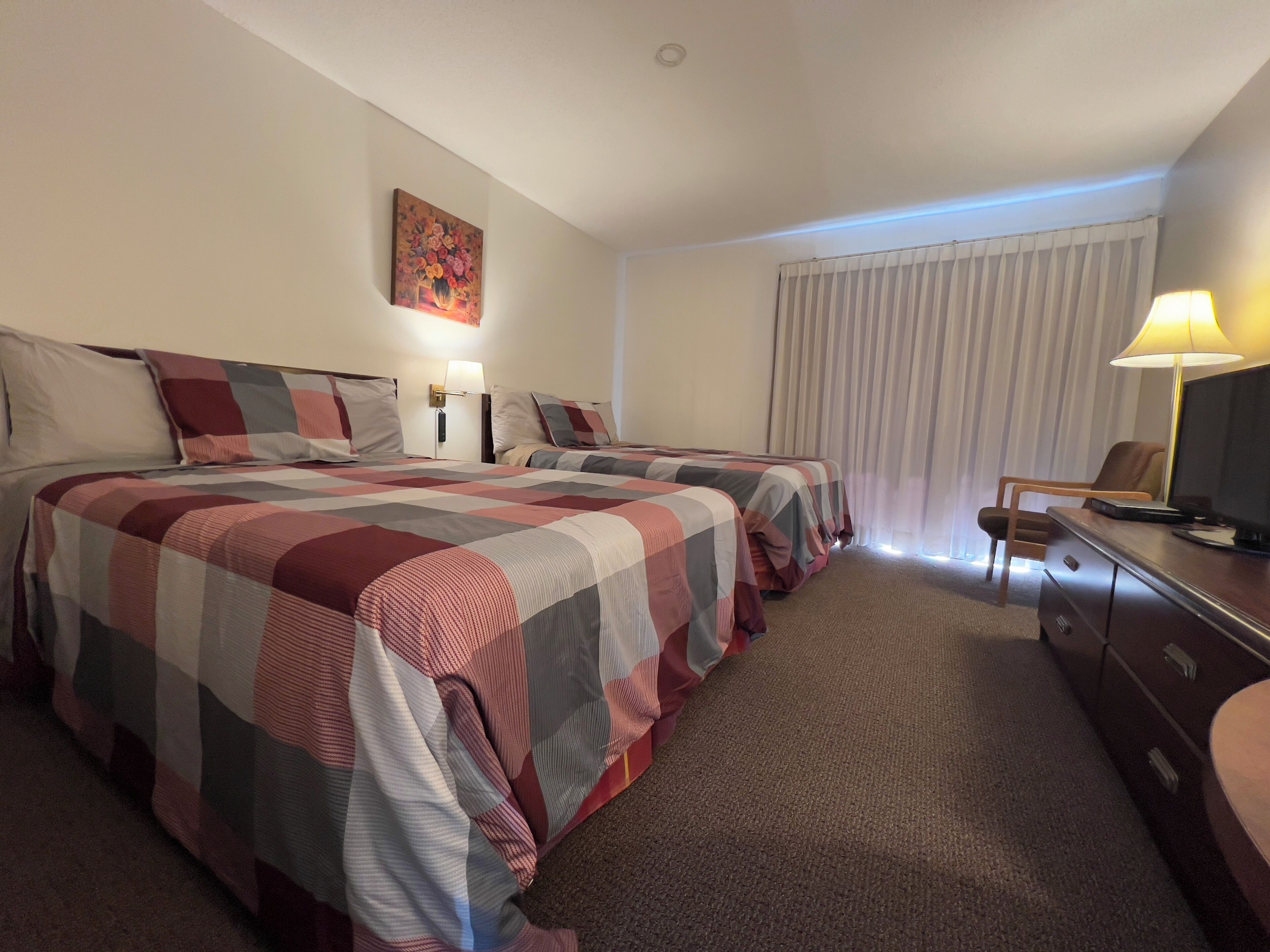 Een hotelkamer met twee bedden, een bureau met lamp, een televisie en een schilderij aan de muur.
