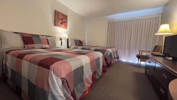 Een hotelkamer met twee bedden, een bureau met lamp, een televisie en een schilderij aan de muur.