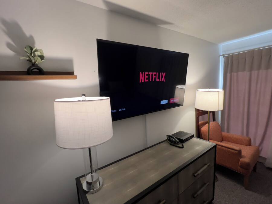 Ein Hotelzimmer mit einem Flachbildfernseher, der das Netflix-Logo anzeigt, einem Schreibtisch mit Lampe, einem Telefon und einem Sessel.