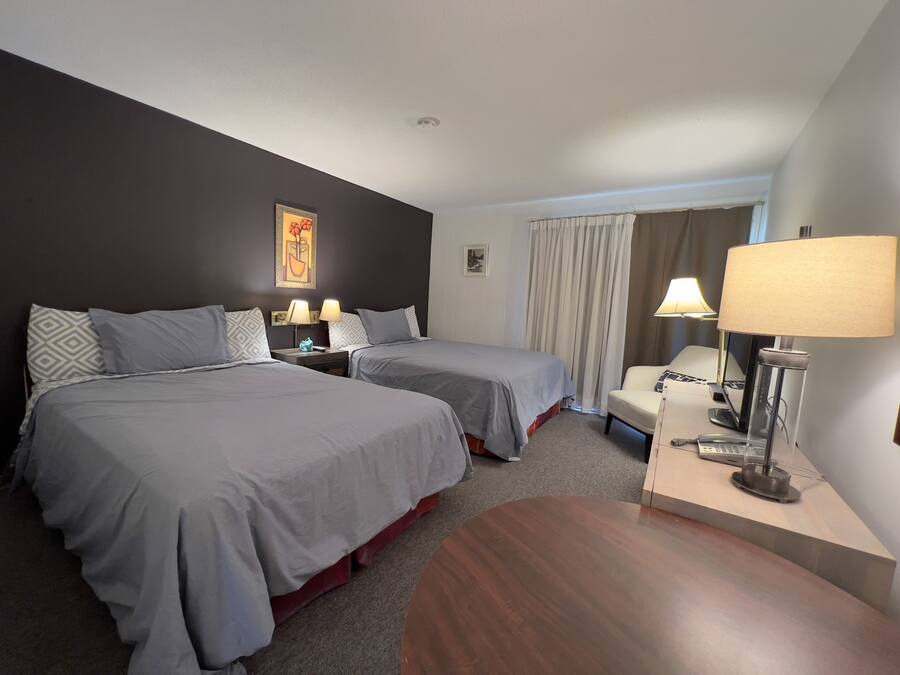 Una habitación de hotel con dos camas, un escritorio con lámpara, una silla y una mesita.