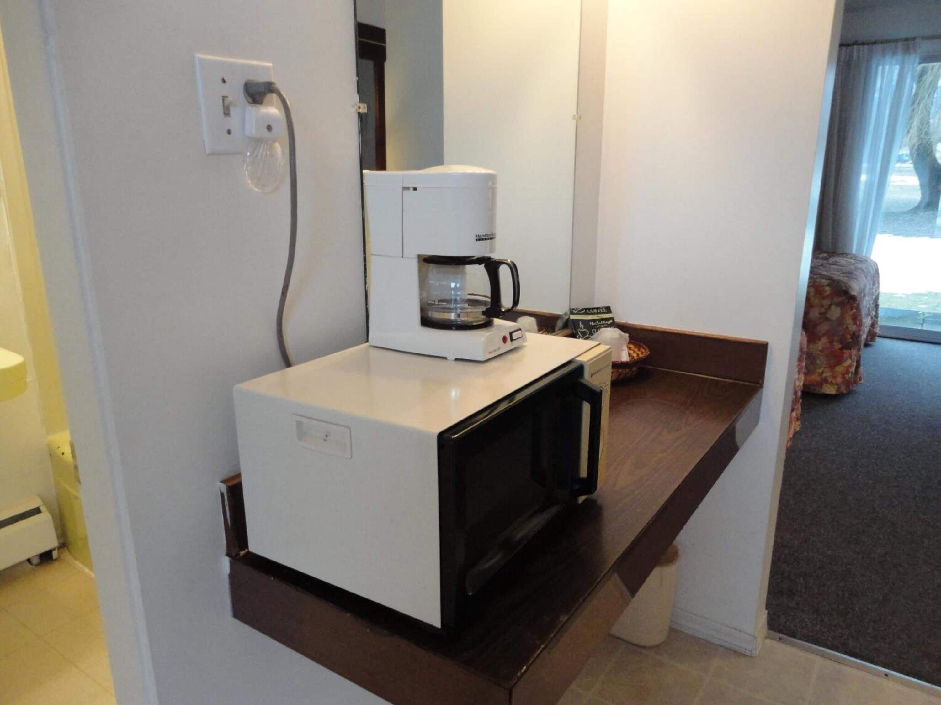 Una kitchenette compacta con cafetera, microondas y refrigerador pequeño.