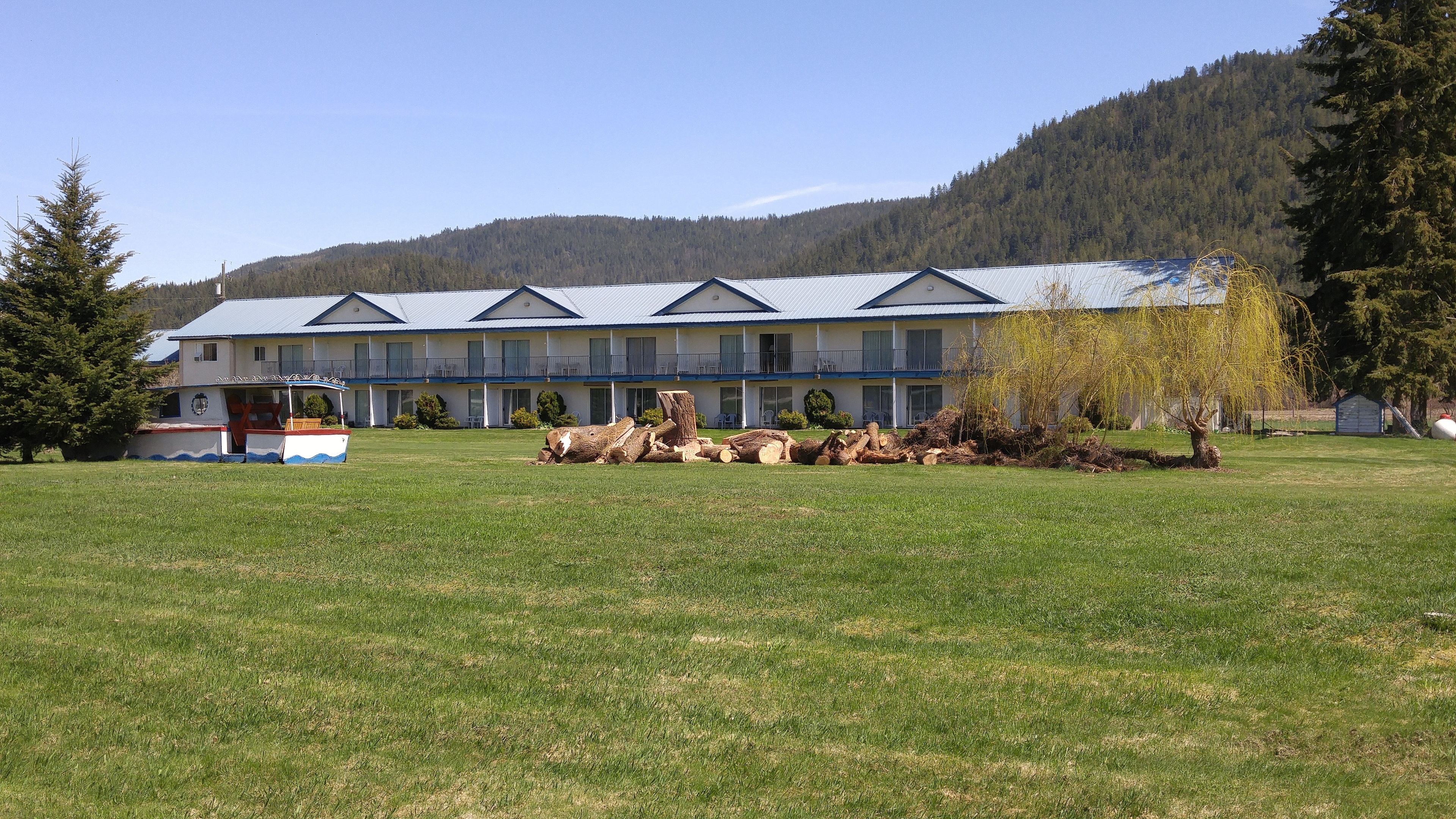 A hotel with a large lawn, a boat, and a forested mountain in the background.