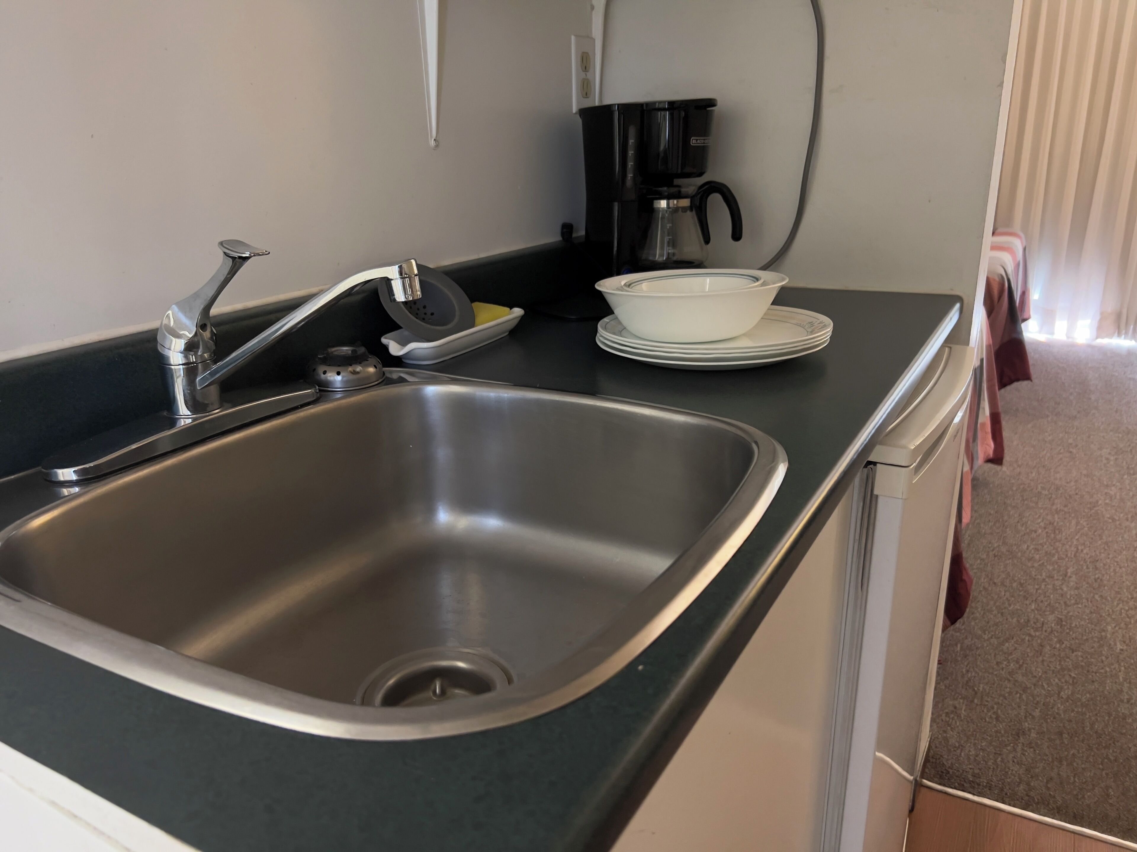 A kitchen with a stainless steel sink, a coffee maker, and stacked white plates.